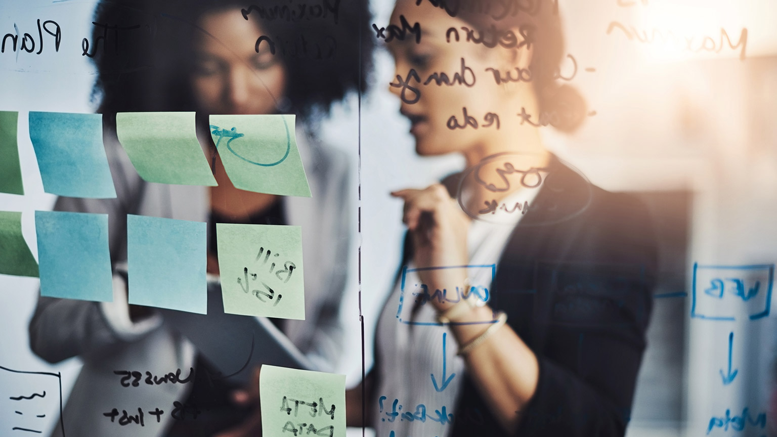 Coworkers writing notes on a glass wall in an office