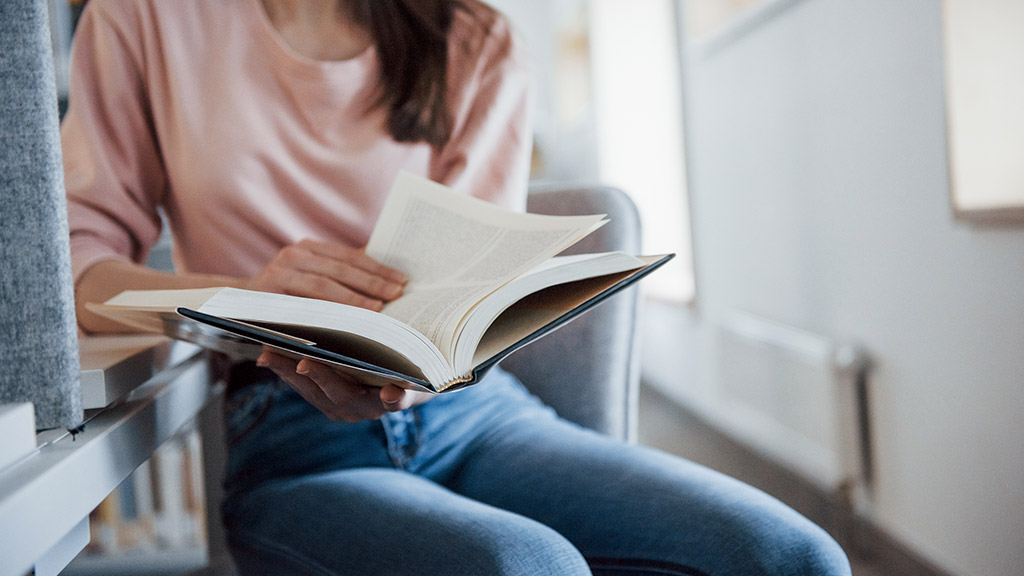 young lady in casual clothes having good time in the library full of books