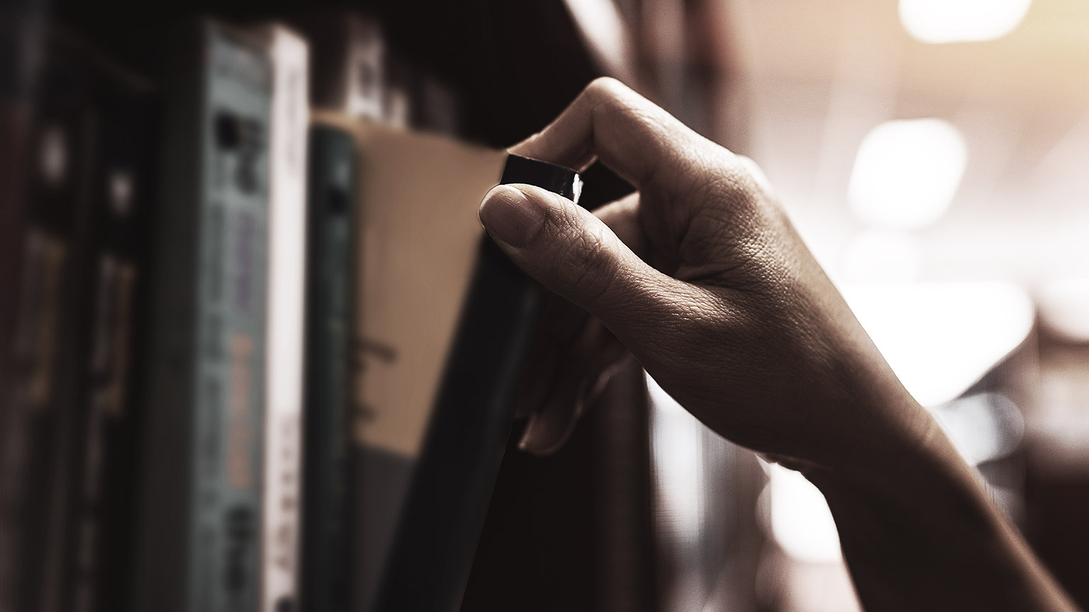 a person's hand getting a book from the library rack