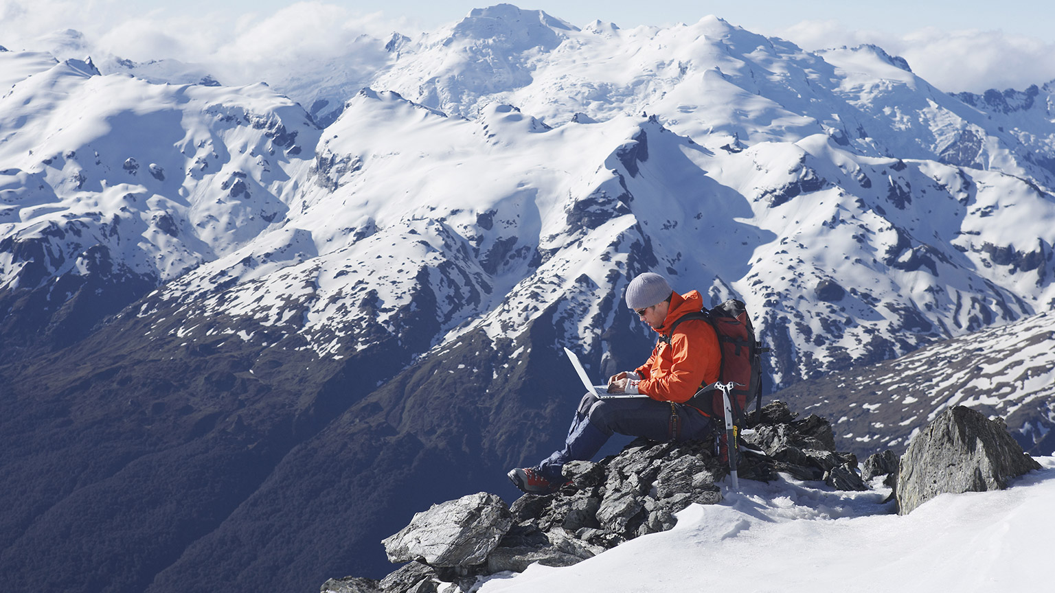 An improbable image of a person working on a laptop on top of a mountain