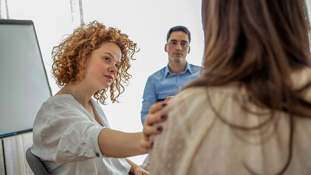 Supportive therapist comforting a young woman who lost his parents in group therapy for people