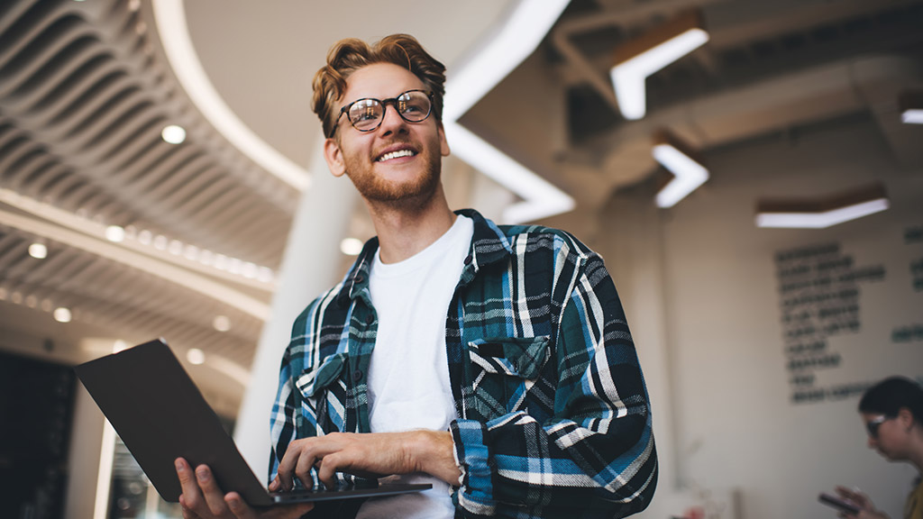  Bottom view of caucasian guy using laptop and looking away in office space