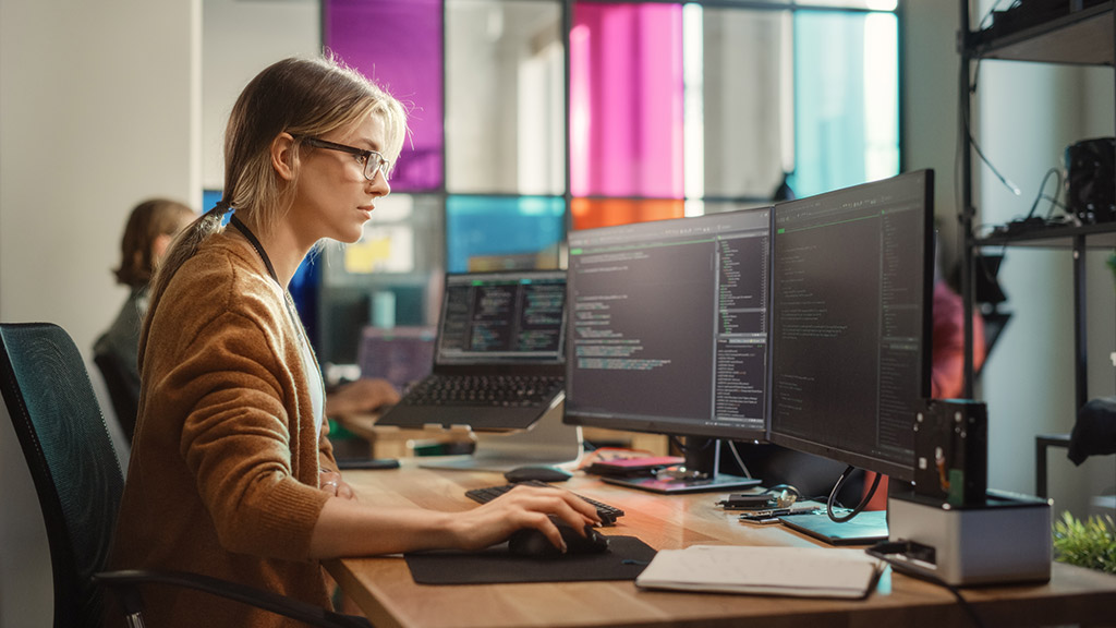 Caucasian Woman Coding on Desktop PC and Laptop Setup