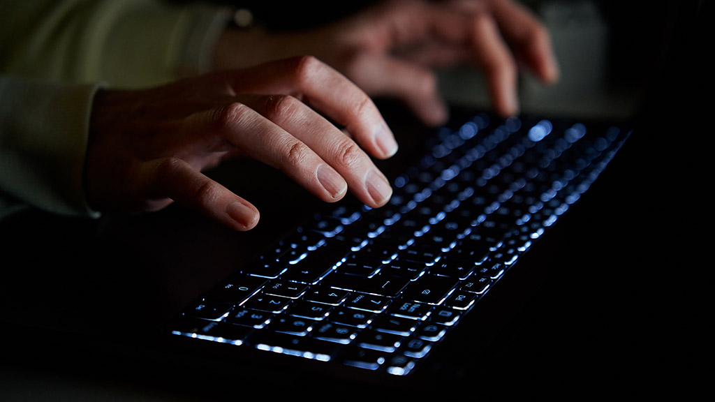 Hands of anonymous person typing on laptop keyboard at night, close up