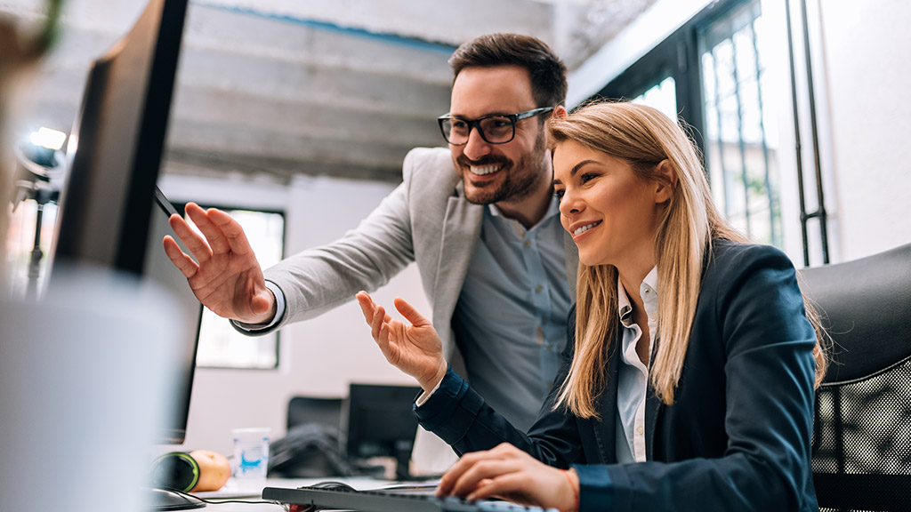 Confident young man standing near whiteboard and shaking hand to his colleague while young woman standing near them and smiling