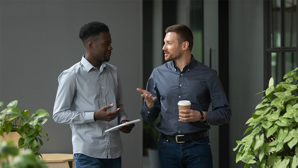 Diverse friendly male partners colleagues talking walking in modern office hallway