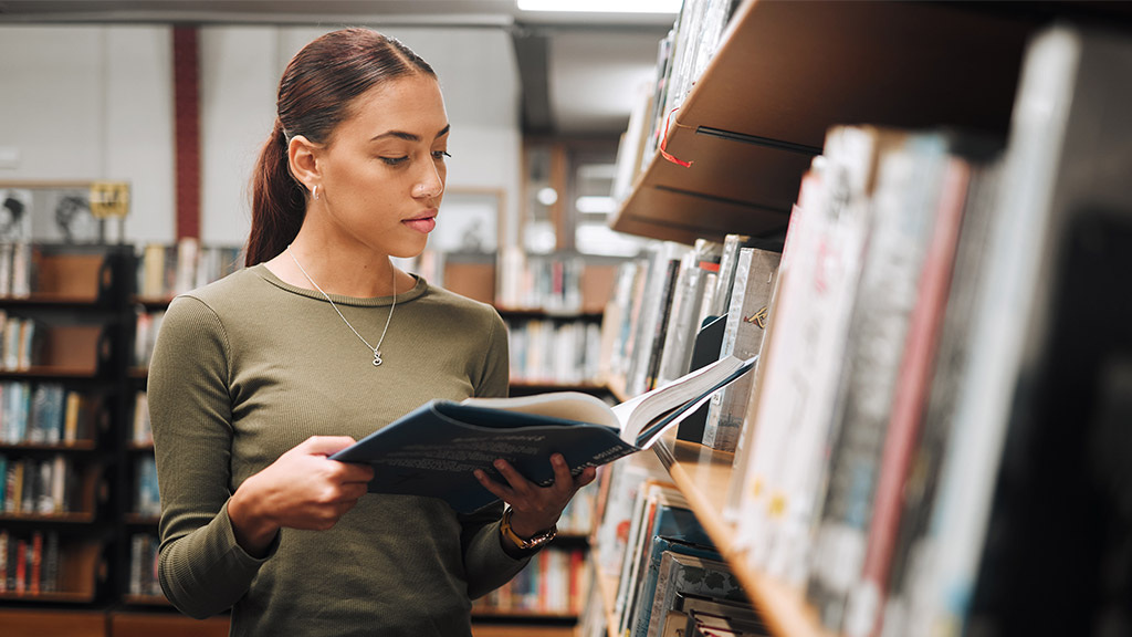 Black woman reading book in a library for education, studying and research in school, university or college campus