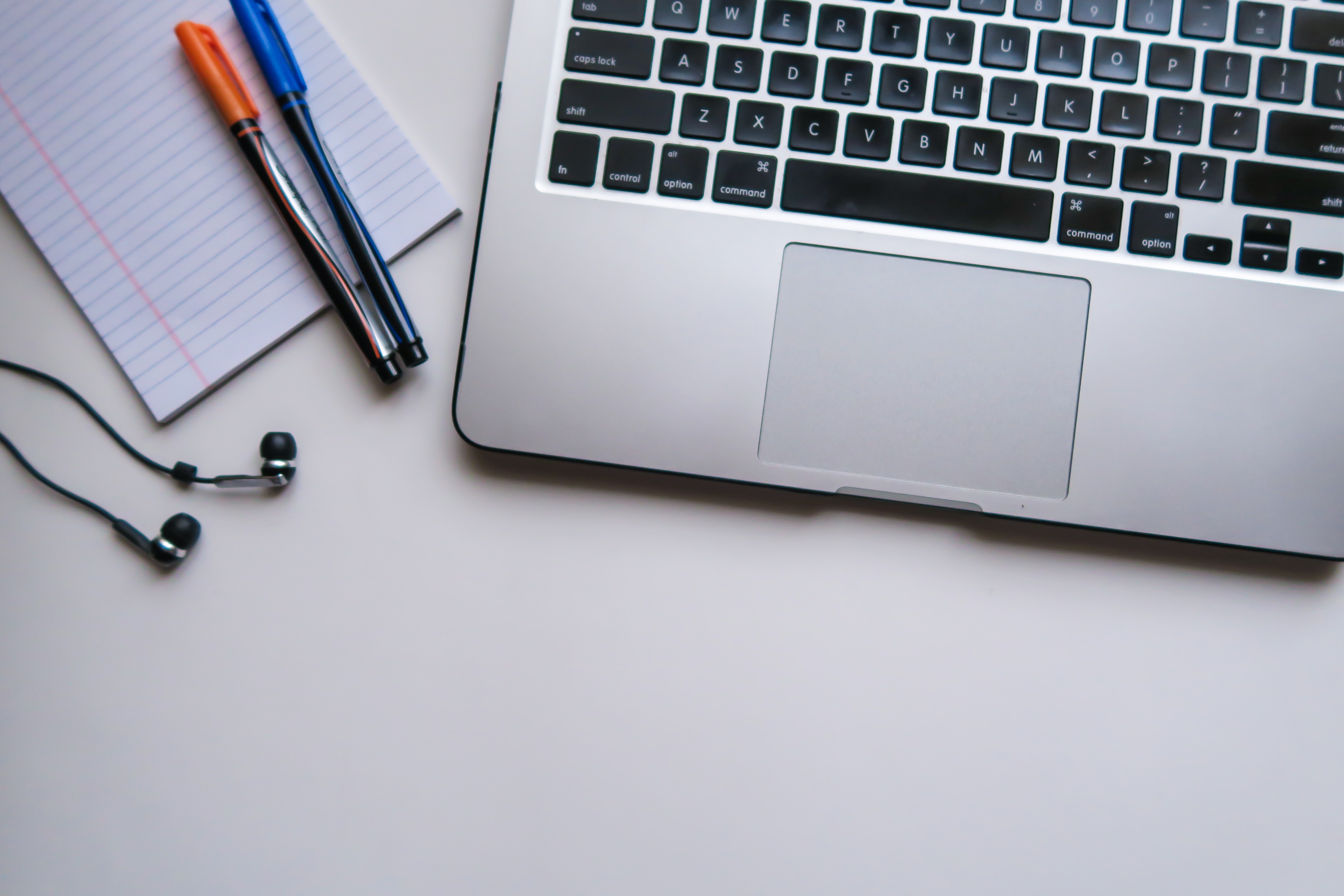 Laptop sitting on desk with notepad and pens