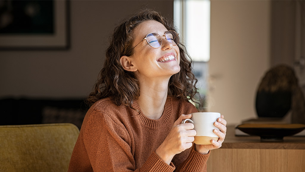 joyful young woman enjoying a cup of coffee at home