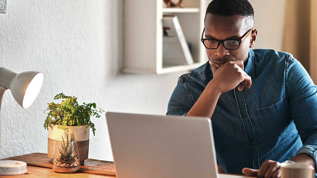 handsome young businessman sitting in his home office and looking contemplative while working on his laptop.