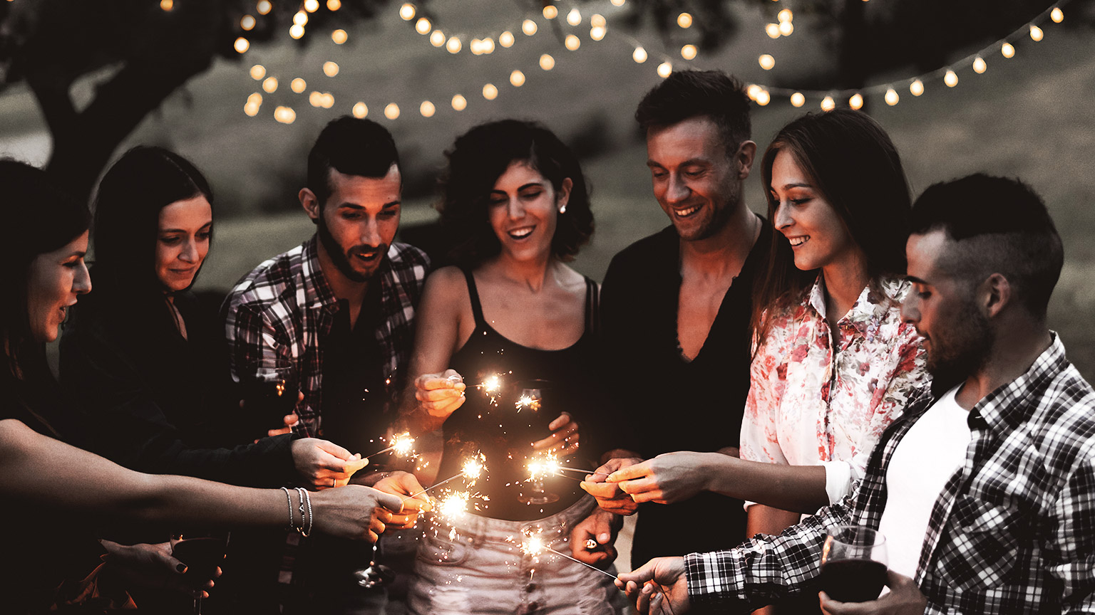 Group of people with different ages and ethnicity, celebrating with sparklers at night outdoors