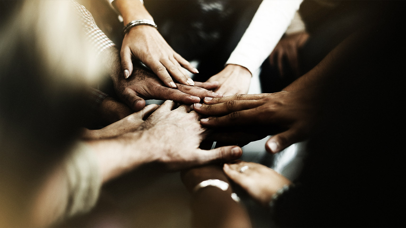 different races and peoples hands stacked on top of each other like a team gesture