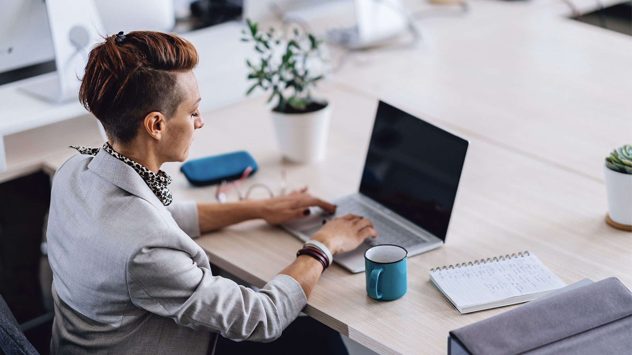 Businesswoman with short hair wearing grey suit sitting in the office and using laptop