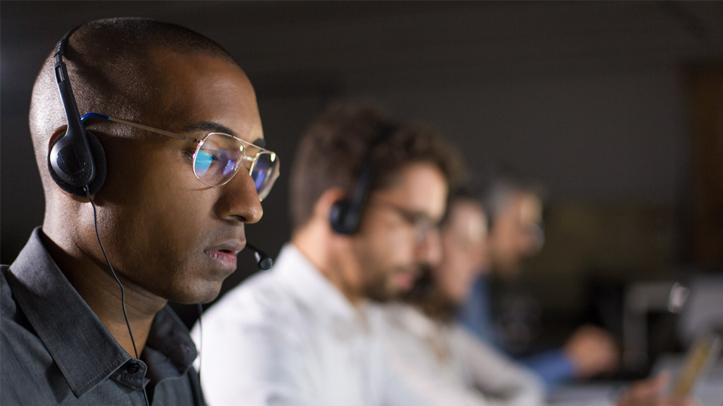 Concentrated call center operator communicating with client. African American young man in eyeglasses looking at laptop while serving client. Call center concept