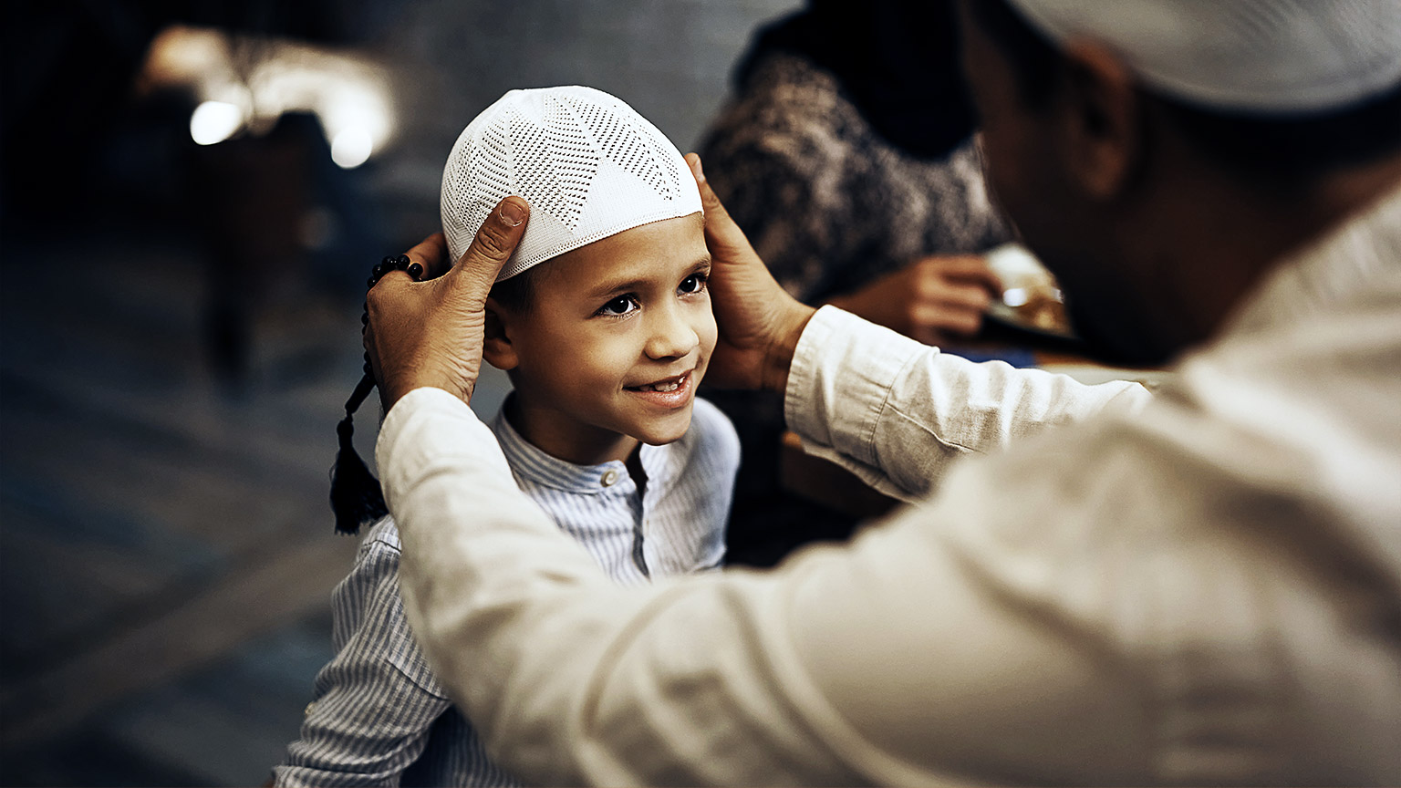 Muslim father holding son's hand while talking to him during dinner in dining room.