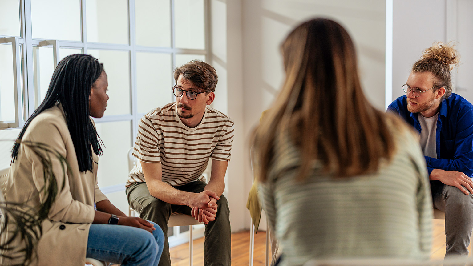 Multiracial group of people sitting on chairs in a circle and discussing some problems together during the therapy session