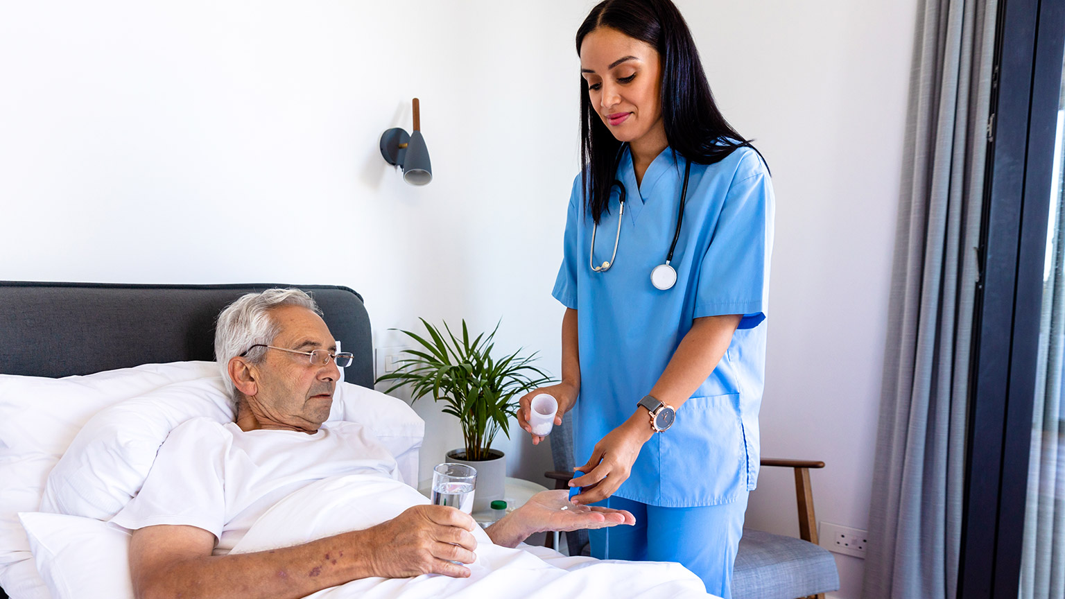 A nurse gives a patient in a hospital bed medication 