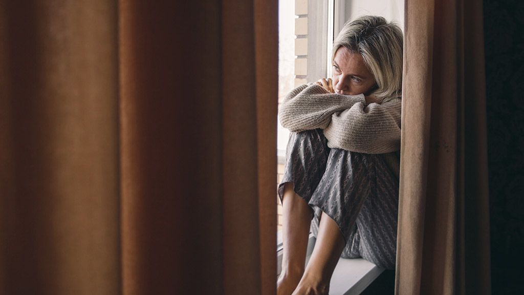 Adult upset woman is sitting by the window.