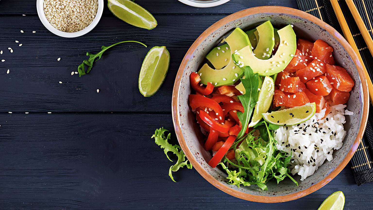 Hawaiian salmon fish poke bowl with rice, avocado, paprika, sesame seeds and lime.