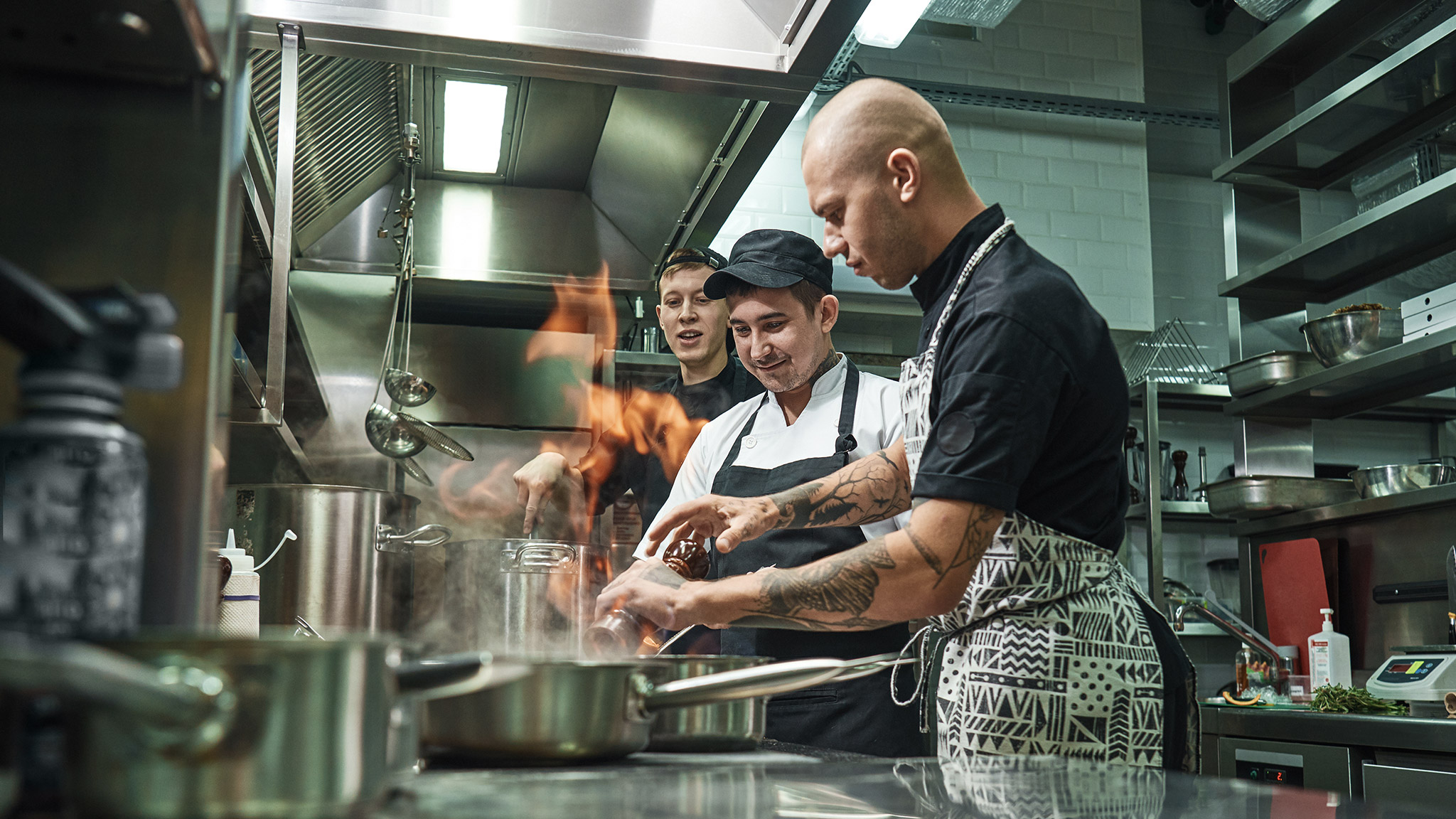 Profesional chef teaching his two young trainees how how to flambe food safely. 