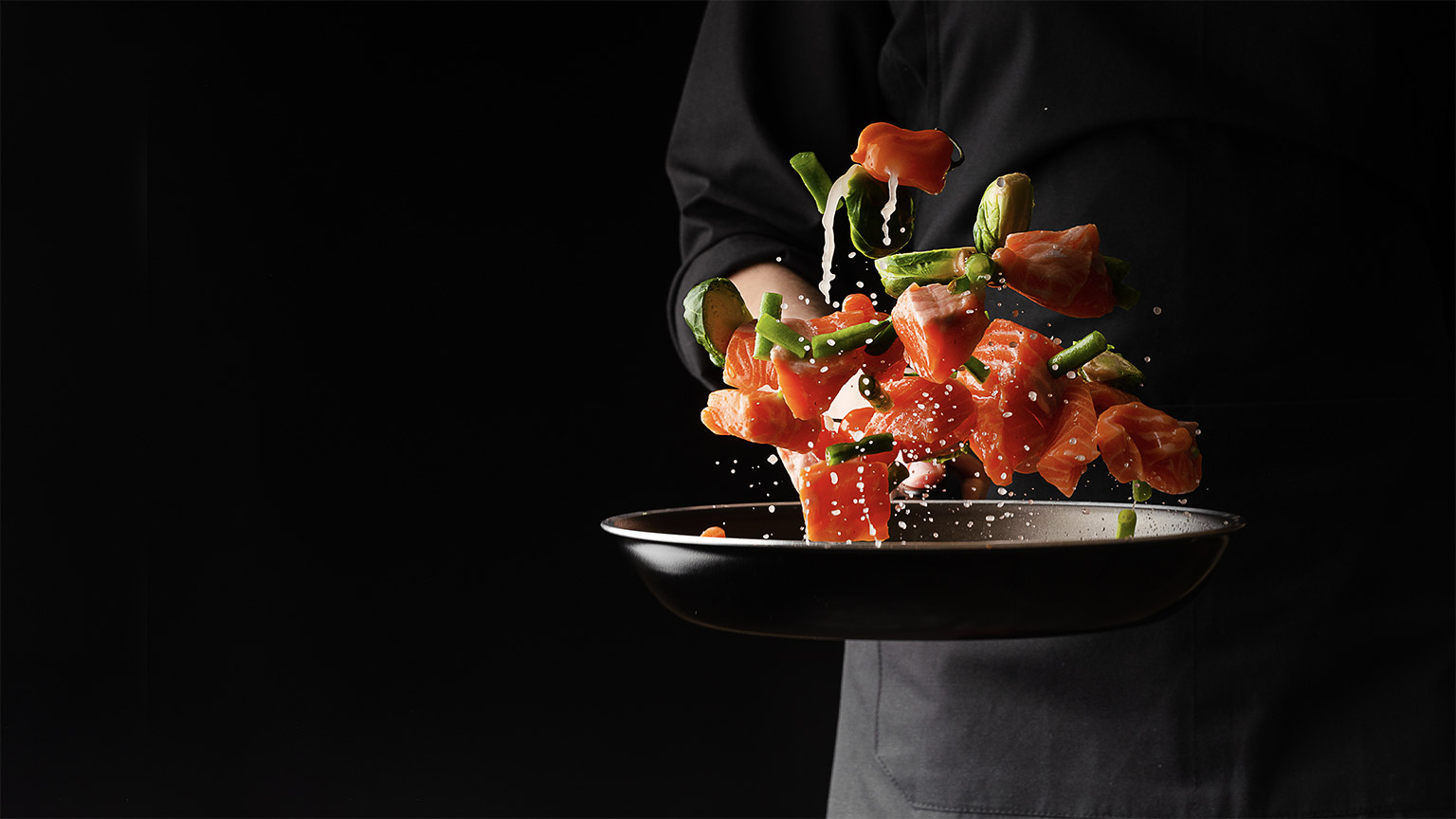 Sea cuisine, Professional cook prepares pieces of red fish, salmon, trout with vegetables.Cooking seafood, healthy vegetarian food and food on a dark background. Horizontal view.