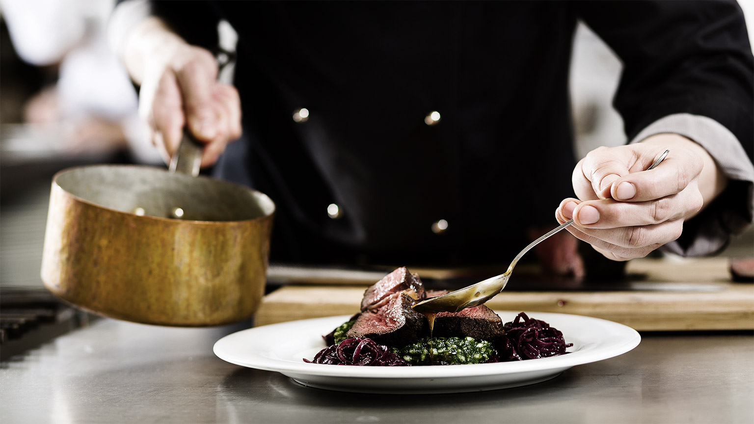 Chef in hotel or restaurant kitchen cooking, only hands, he is working on the sauce for the food as saucier, a Risotto