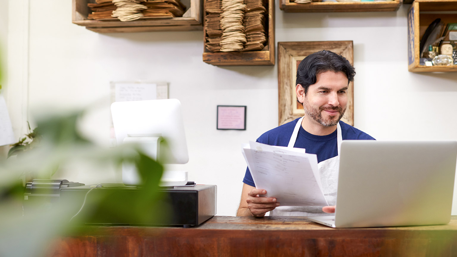 a man working on laptop behind sales desk of his small business store