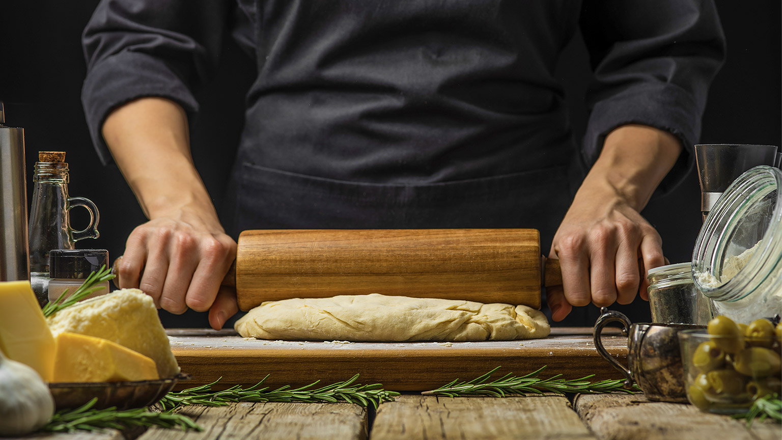 The chef shakes the dough on the cutting board with a rolling pin.