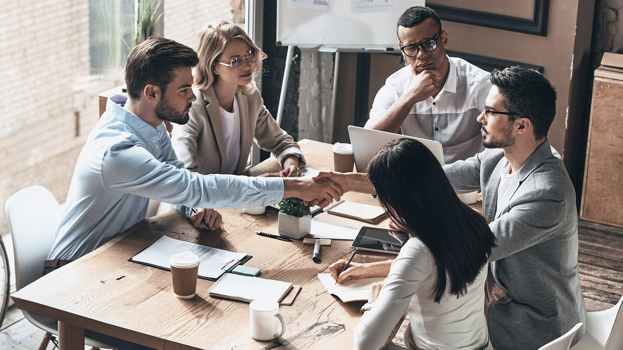 young men shaking hands while having business meeting in office