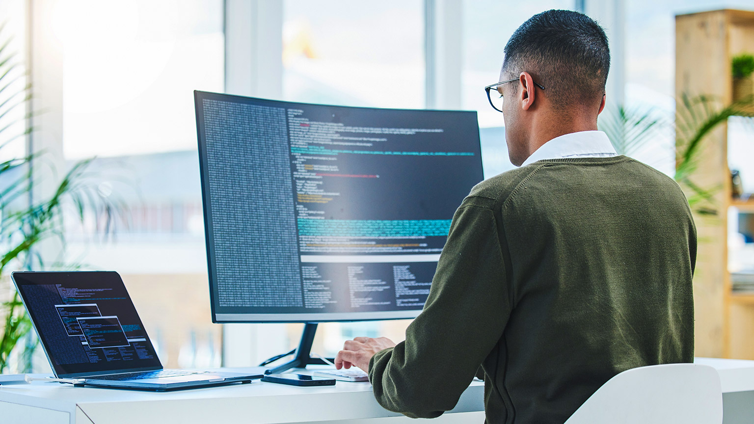 An IT person working on multiple screens in an office