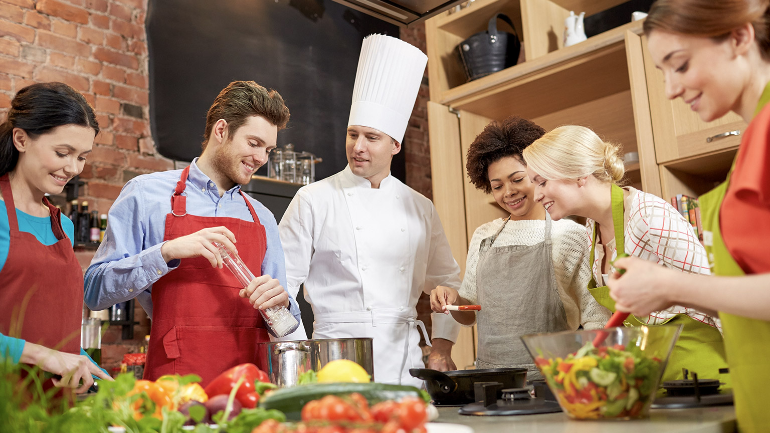 cooking class, culinary, food and people concept - happy group of friends and male chef cook cooking in kitchen