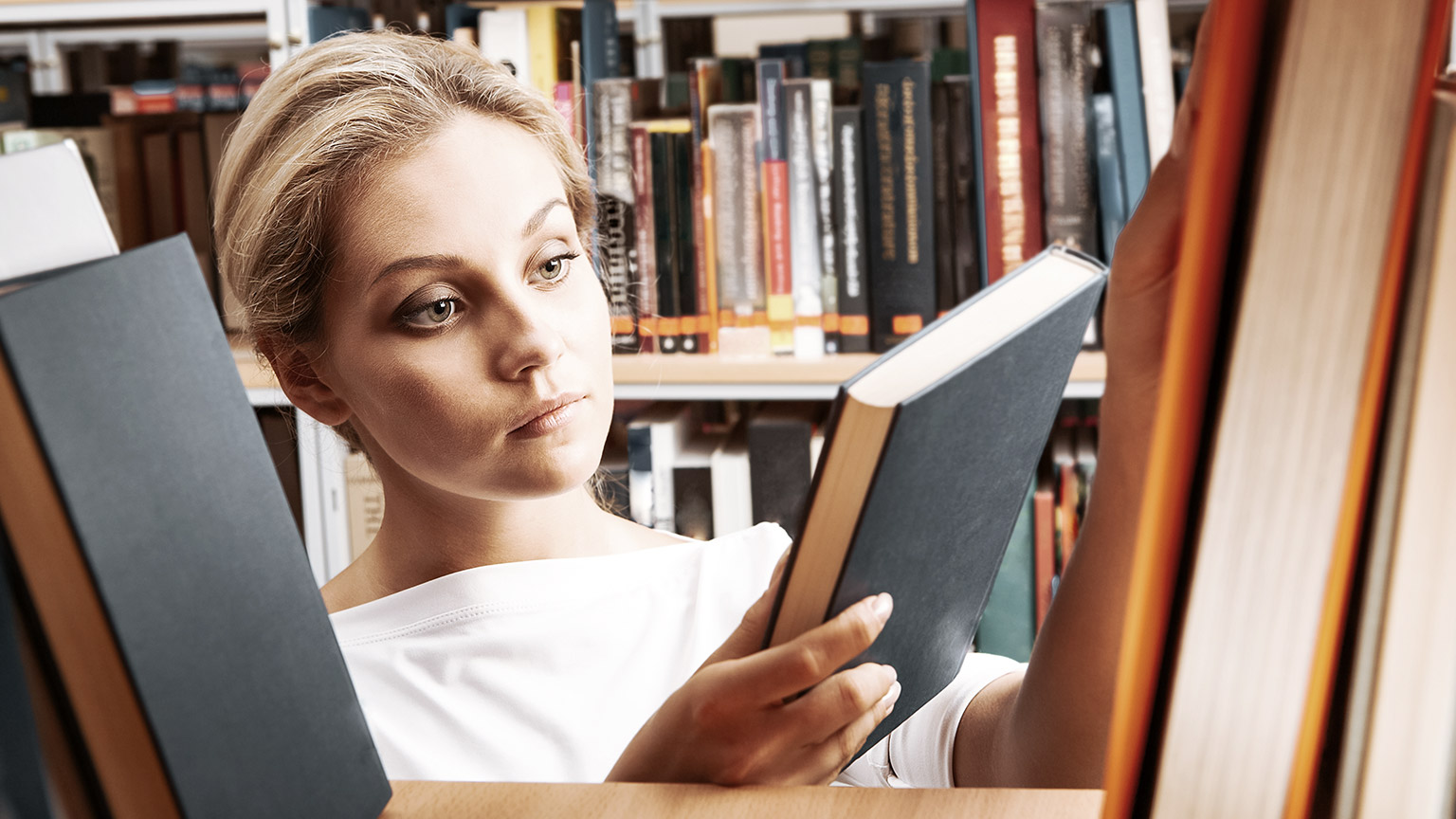 Student taking out books from library shelf