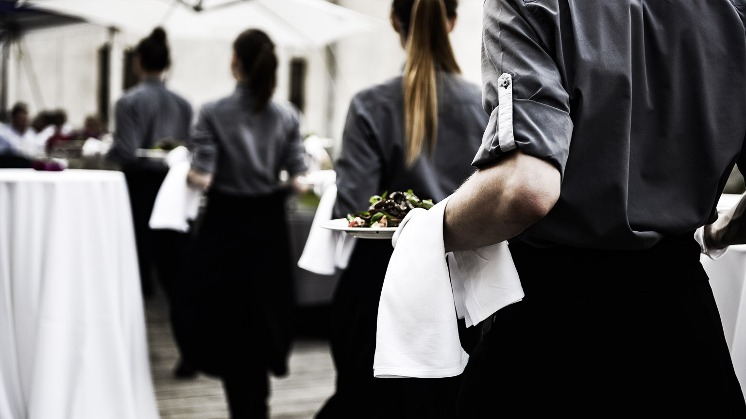 Waiter carrying plates with meat dish on some festive event