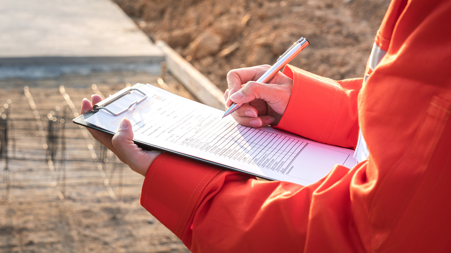 A person writing on a clipboard on a construction site