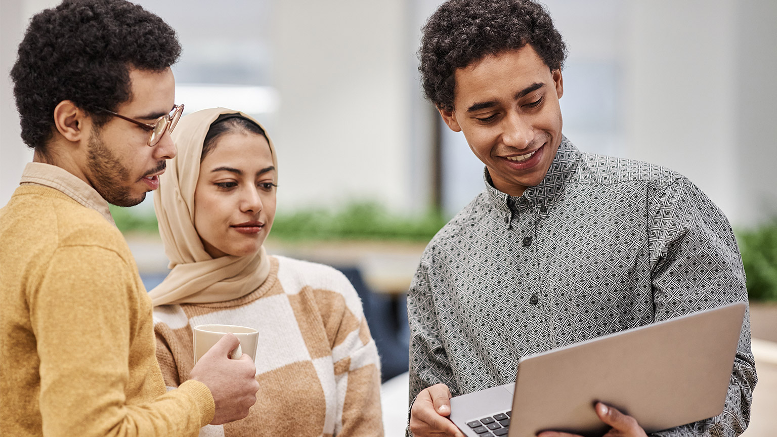 Group of modern Middle Eastern professionals holding laptop while discussing work project in office