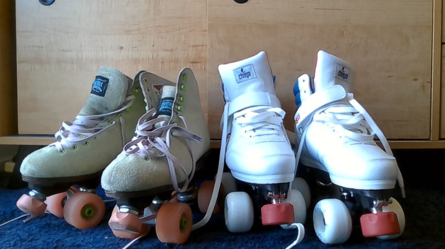 A pair of green roller skates next to a pair of white roller skates.