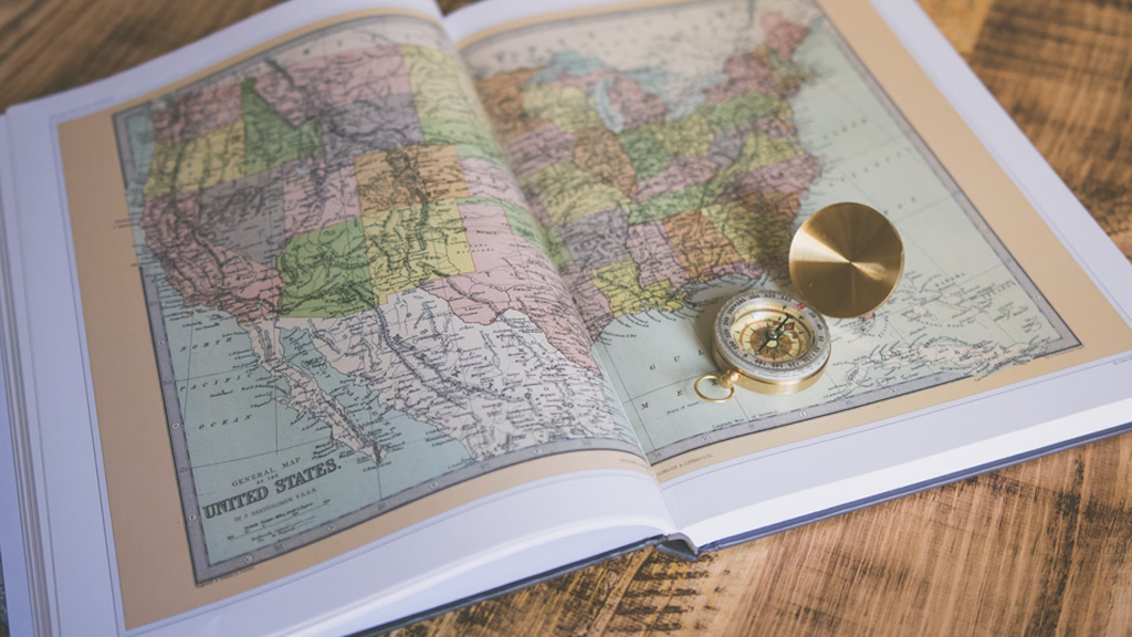 an open book showing a map of the united states of america with a gold compass sat on top of the book