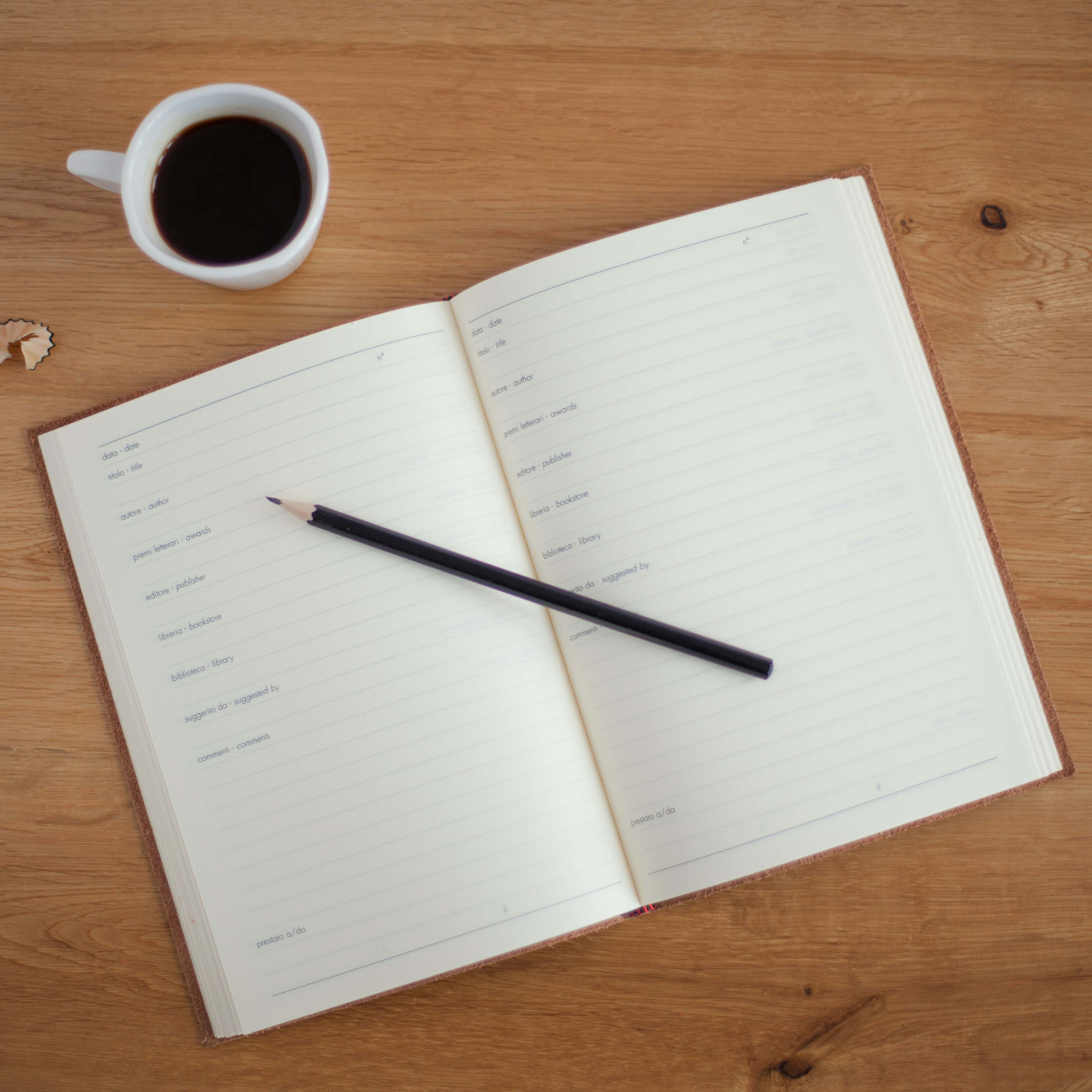 Open notepad with a pencil on top, Sitting on a wooden table with a cup of coffee next to the notebook