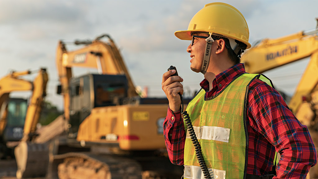 Asian engineers use walky talky with team for earthmoving project by excavator. foreman use laptop for construction project heavy digger