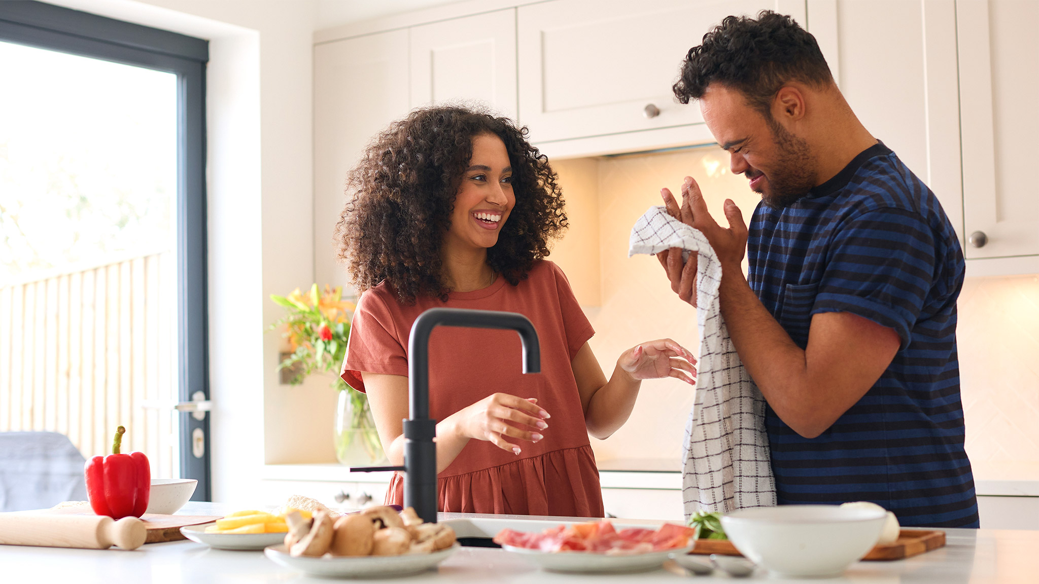 Couple At Home With Man With Down Syndrome And Woman Washing Hands Before Preparing Meal In Kitchen