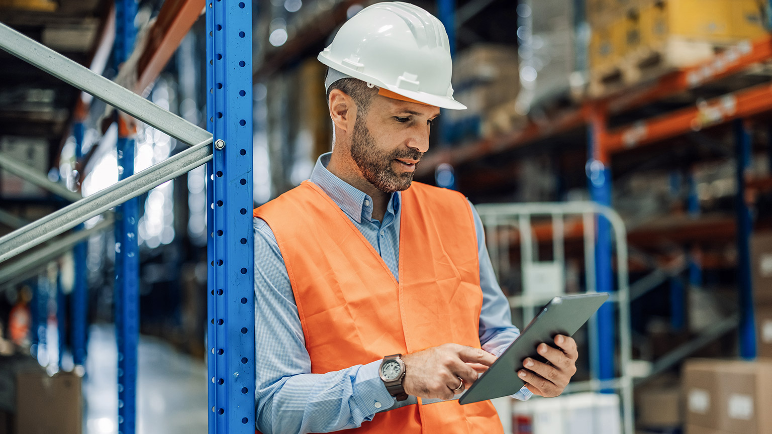 Warehouse manager wearing reflective vest and protective helmet using digital tablet