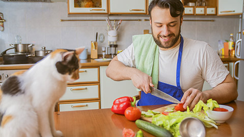 a man cooks in the kitchen beside him sits a funny beautiful cat