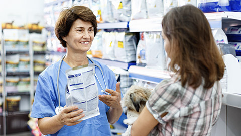 cheerful positive female veterinarian recommending pet food to young woman visiting pet store with her puppy