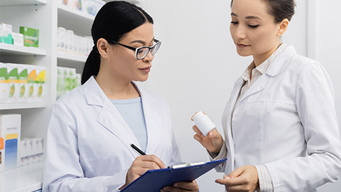 asian colleague in glasses writing on clipboard in drugstore