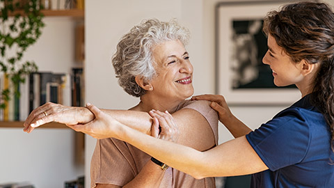 senior woman doing exercise at home with physiotherapist