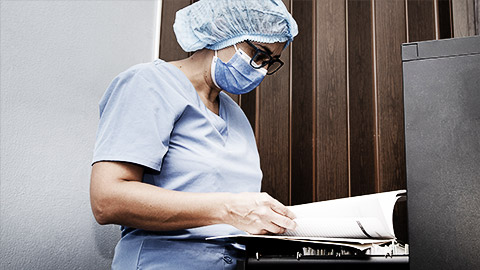 Nurse reviewing medical record in clinic filing cabinet