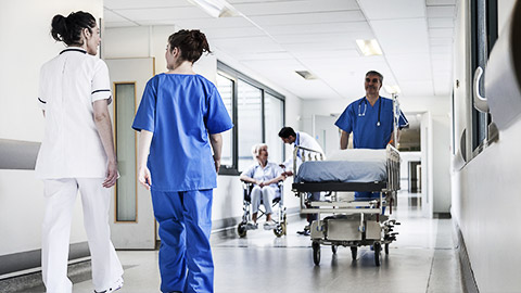 Male nurse pushing stretcher gurney bed in hospital corridor with doctors & senior female patient