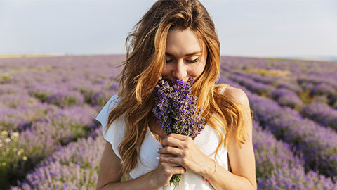 woman in dress holding bouquet of flowers while walking outdoor through lavender field