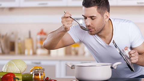 man tasting soup from the pan while standing in the kitchen