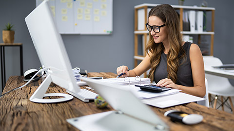 Smiling Businesswoman Calculating Tax At Desk In Office